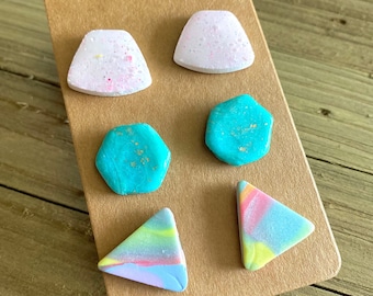 May include: Set of six colorful polymer clay earrings. The earrings are in the shapes of a hexagon, a triangle, and a rounded rectangle. The colors are turquoise, pink, yellow, and blue.