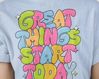 Może przedstawiać: Jasnoniebieska koszulka z napisem "GREAT THINGS START TODAY" w kolorowej, bąbelkowej czcionce. Tekst jest obrysowany na czarno i ma kolory różowy, pomarańczowy, zielony i niebieski. Koszulka ma krótkie rękawy.