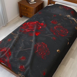 May include: A black twin-size bedspread featuring a pattern of large red roses and gold accents. The floral design is set against a dark background, creating a striking contrast. The bedspread is draped over a wooden bed frame.