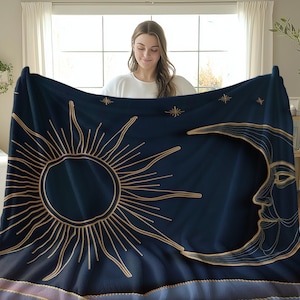 Könnte beinhalten: Eine marineblaue Tagesdecke mit einem goldenen Sonnen- und Monddesign. Die Sonne hat einen kreisförmigen Mittelpunkt und Strahlen, die sich nach außen erstrecken. Der Mond ist sichelförmig mit einem Gesicht.