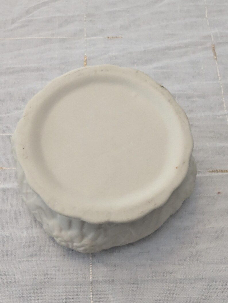 May include: A white ceramic bowl with a scalloped edge. The bowl has a circular base and a textured exterior. The bowl is sitting on a white, textured surface.