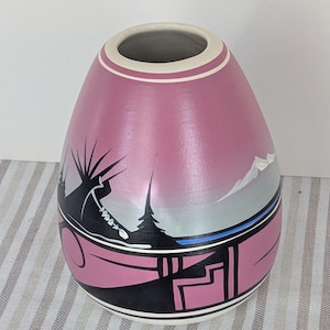 Peut inclure: Un vase en céramique rose avec un motif de paysage. Le vase présente une scène de montagne en noir et blanc avec un ciel bleu et un motif géométrique noir à la base. Le bord supérieur a des rayures blanches et roses.