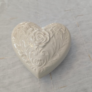 May include: White ceramic heart-shaped trinket box with an embossed floral design.