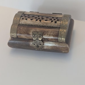 May include: A small, rectangular box made of brown wood with intricate carvings and brass accents. The box has a hinged lid with a decorative brass latch.