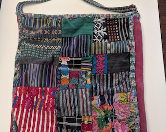 Puede incluir: Un bolso tote de patchwork con una correa burdeos y un diseño de patchwork colorido. El bolso está hecho de diferentes telas y tiene una variedad de patrones, incluyendo rayas, flores y formas geométricas.