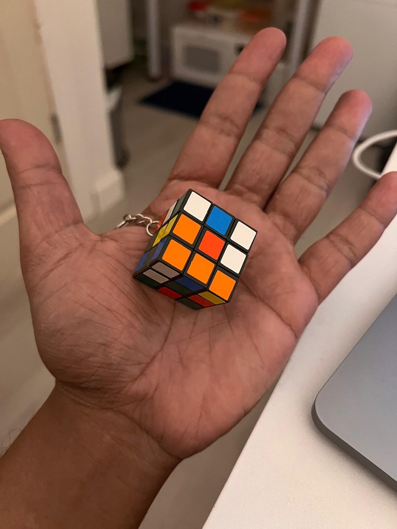 Puede incluir: Un llavero de cubo de Rubik en miniatura. El cubo presenta la cl&aacute;sica disposici&oacute;n de cuadrados de colores: blanco, amarillo, naranja, rojo, azul y verde. El llavero est&aacute; sujeto a una cadena de color plateado.