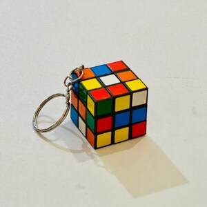 Puede incluir: Un llavero de cubo de Rubik en miniatura. El cubo presenta un dise&ntilde;o cl&aacute;sico con cuadrados coloridos en rojo, azul, amarillo, verde, naranja y blanco. El llavero tiene un anillo de color plateado adjunto al cubo.