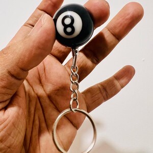 May include: A black and white eight ball keychain. The ball has a white number eight on a black background. The keychain has a silver chain and a large silver ring.