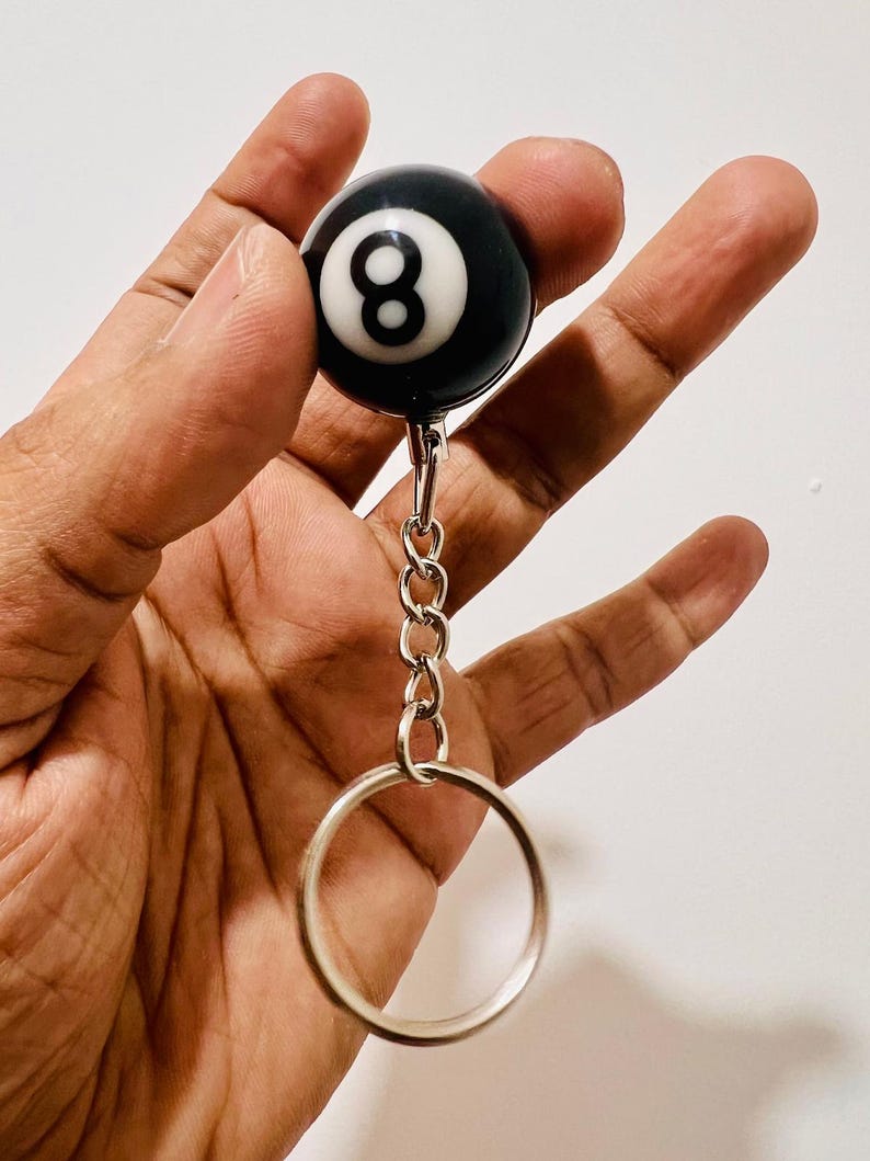 May include: A black and white eight ball keychain. The ball has a white number eight on a black background. The keychain has a silver chain and a large silver ring.