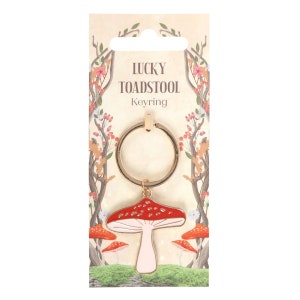 May include: A gold-tone keyring with a red and white mushroom charm. The charm has white spots and a pink stem. The keyring is packaged on a card with the text "Lucky Toadstool Keyring".