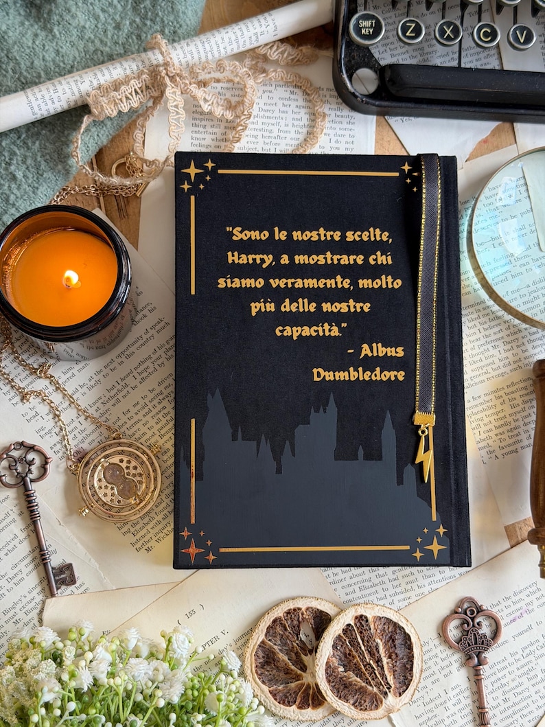 May include: A black journal with gold accents and the quote "Sono le nostre scelte, Harry, a mostrare chi siamo veramente, molto pi&ugrave; delle nostre capacit&agrave;." A gold lightning bolt charm hangs from the bookmark. The journal is surrounded by vintage items.