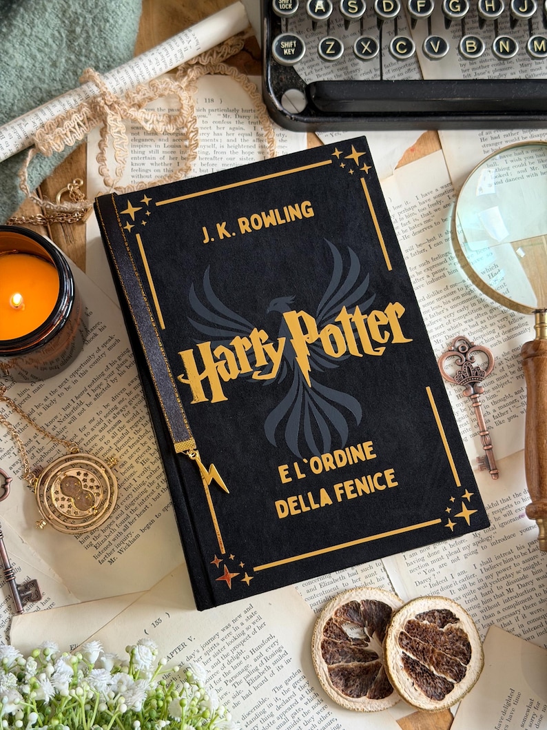 May include: A black hardcover book titled "Harry Potter and the Order of the Phoenix" by J.K. Rowling. The book features gold lettering and a phoenix illustration. The image includes a candle, a magnifying glass, and vintage keys.