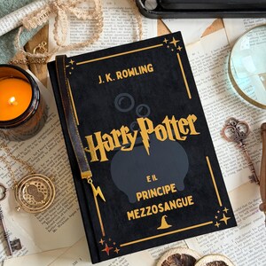 May include: A black hardcover book titled "Harry Potter e il Principe Mezzosangue" by J.K. Rowling. The book has gold lettering and a black cauldron graphic. A gold bookmark and a candle are visible.