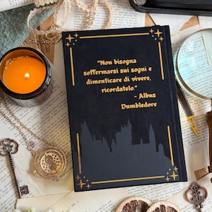 May include: A black book with gold lettering and a castle silhouette, featuring a quote by Albus Dumbledore. The image includes a lit candle, a necklace, keys, and dried orange slices, creating a vintage aesthetic.