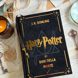 May include: A black hardcover book with gold lettering that reads "Harry Potter e I Doni Della Morte" by J.K. Rowling. The book has a gold bookmark and is surrounded by vintage items.