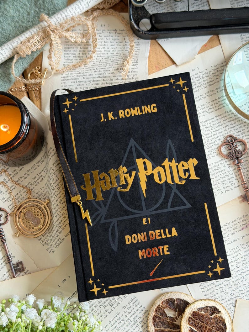 May include: A black hardcover book with gold lettering that reads "Harry Potter e I Doni Della Morte" by J.K. Rowling. The book has a gold bookmark and is surrounded by vintage items.