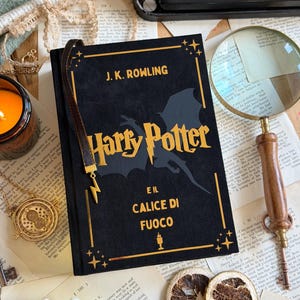 May include: A black hardcover book titled "Harry Potter and the Goblet of Fire" by J.K. Rowling, with gold lettering and a lightning bolt bookmark. The book is on a table with vintage items.
