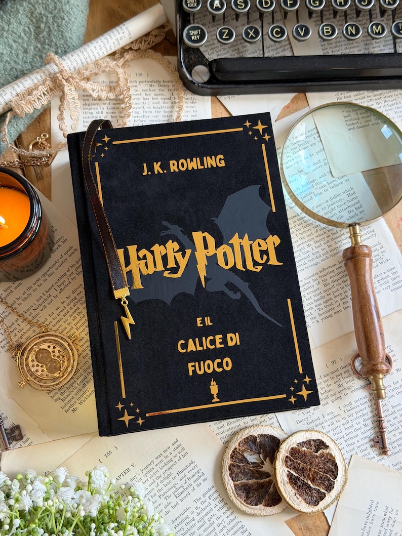 May include: A black hardcover book titled "Harry Potter and the Goblet of Fire" by J.K. Rowling, with gold lettering and a lightning bolt bookmark. The book is on a table with vintage items.