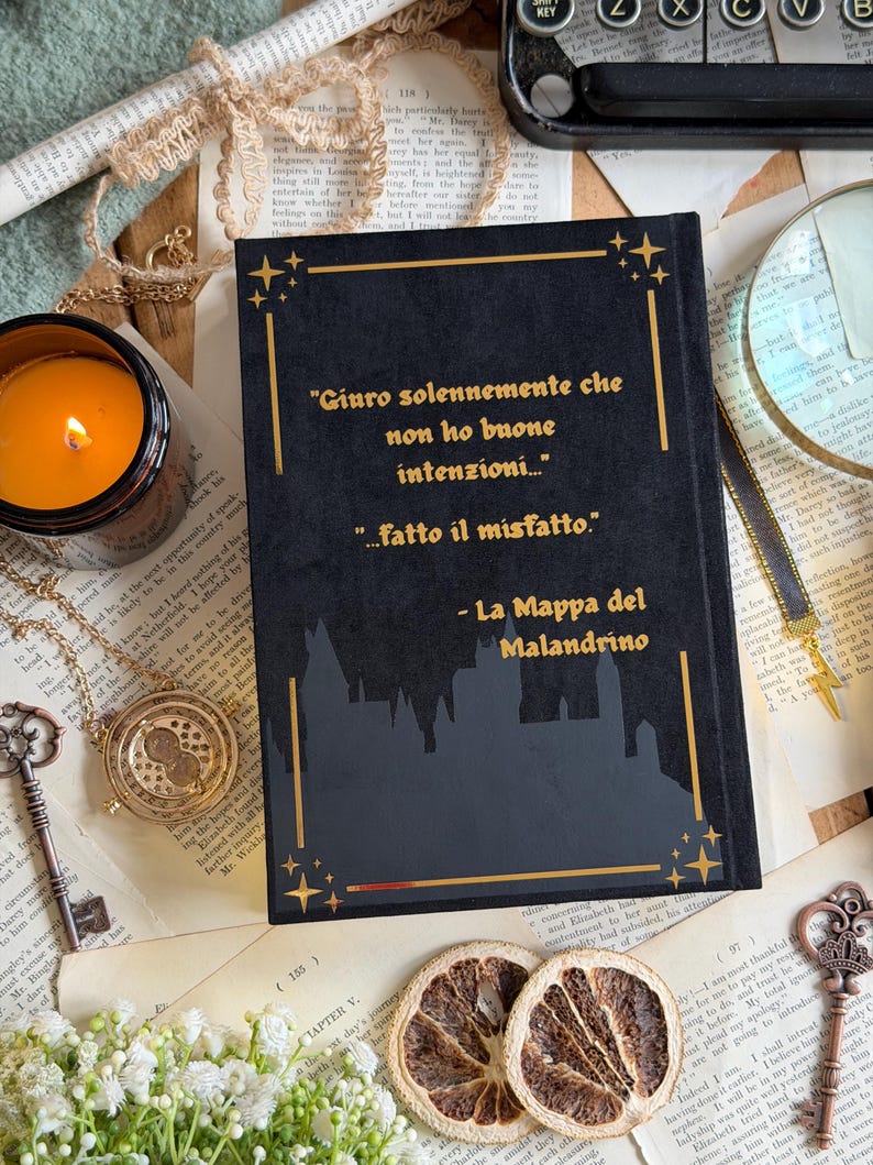 May include: A black book with gold lettering and a silhouette of a castle. The text reads "Giuro solennemente che non ho buone intenzioni... ...fatto il misfatto." and "La Mappa del Malandrino."