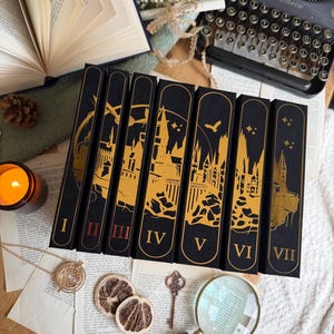 May include: Seven black books with gold castle illustrations and Roman numerals I to VII. The books are displayed with a magnifying glass, dried orange slices, and a vintage key on a wooden surface.