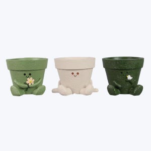 May include: Three small ceramic planters shaped like cartoon characters. The planters are green, white, and green. Each planter has a different facial expression and a small detail, such as a flower or a bird.