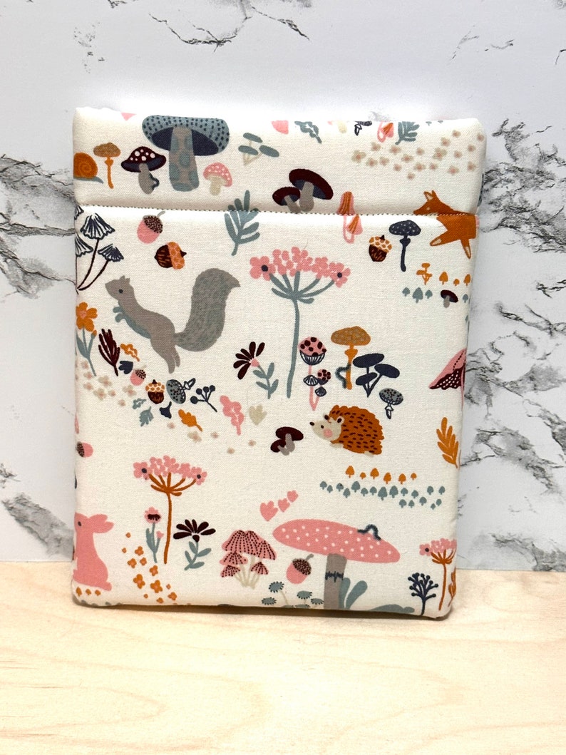 May include: A white fabric pouch with a woodland pattern featuring mushrooms, squirrels, hedgehogs, and other forest creatures. The pouch has a brown zipper and a white background.