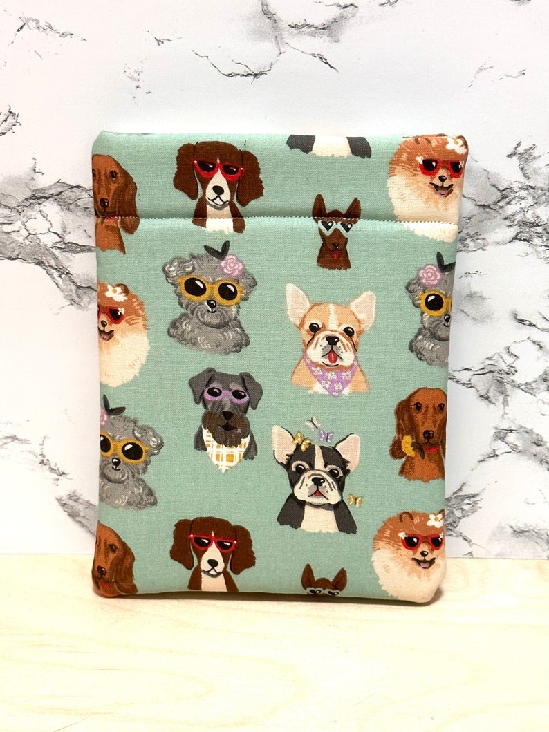 May include: A teal blue fabric pouch with a repeating pattern of dogs wearing sunglasses. The dogs are various breeds and colours, including a dachshund, a French bulldog, a Pomeranian, and a Schnauzer.