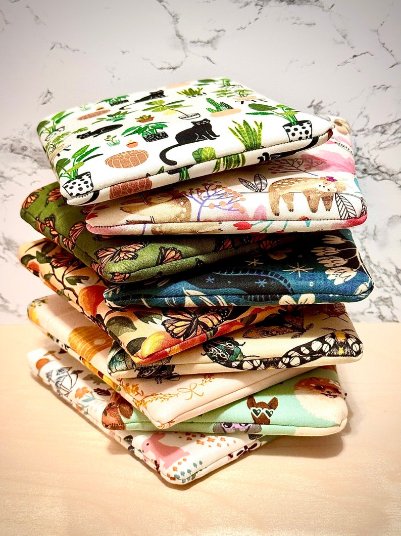 May include: A stack of eight colourful fabric pouches with various patterns, including plants, animals, and geometric designs. The pouches are made of a soft, quilted fabric and have a zipper closure.