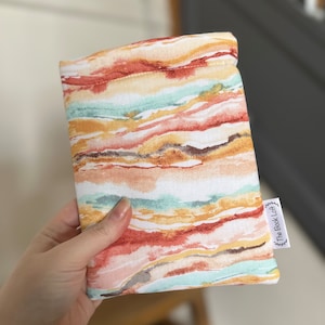 May include: A white fabric pouch with a colorful abstract pattern in shades of orange, yellow, green, and pink. The pouch has a white label with the text "The Book Loft" printed on it.