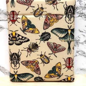 May include: A beige fabric pouch with a repeating pattern of colourful butterflies and beetles. The pouch has a zipper closure and a cream-coloured background.