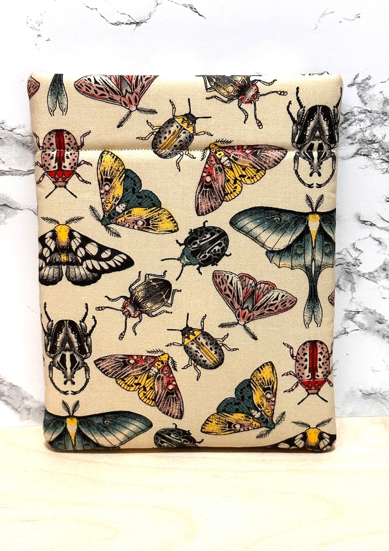May include: A beige fabric pouch with a repeating pattern of colourful butterflies and beetles. The pouch has a zipper closure and a cream-coloured background.