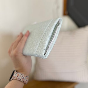 K&ouml;nnte beinhalten: Eine hellgr&uuml;ne Clutch mit einem wei&szlig;en Blumenmuster. Die Clutch ist geschlossen und hat einen Rei&szlig;verschluss.