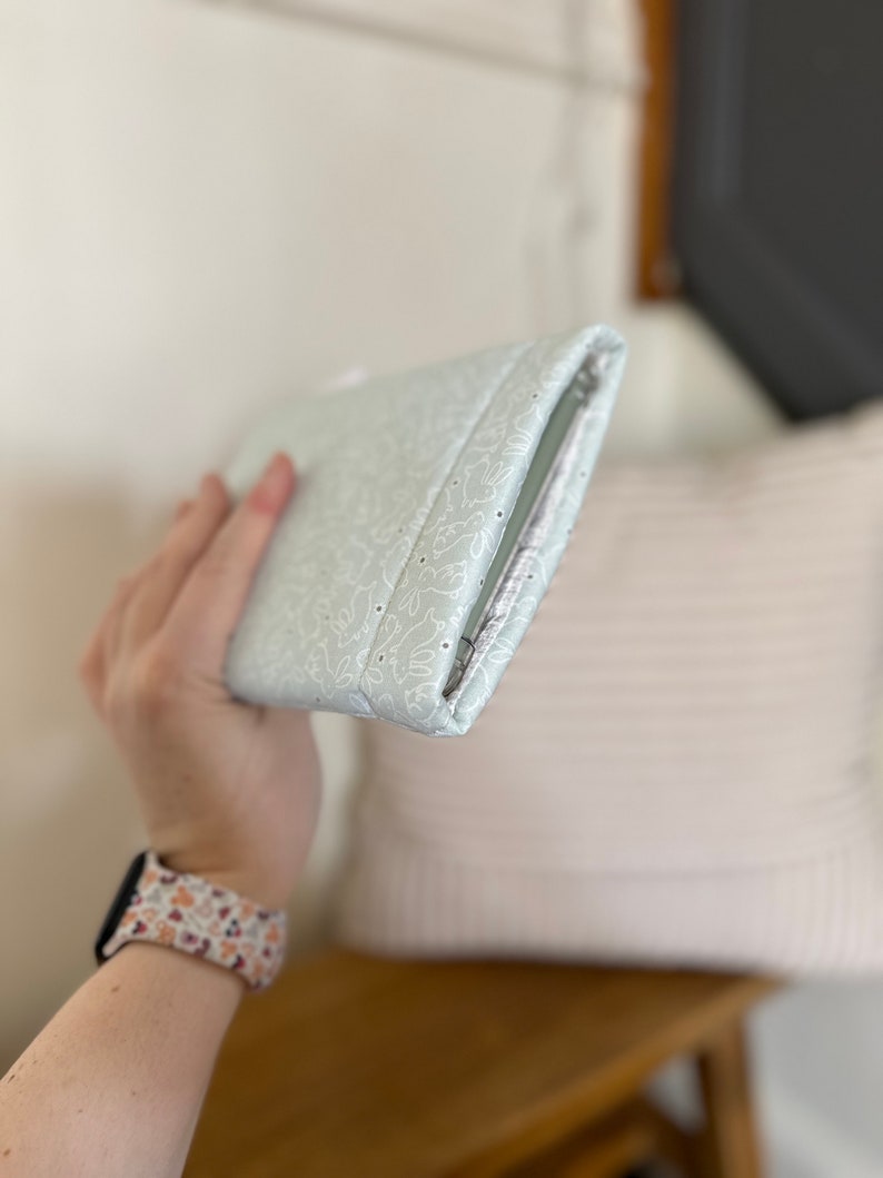 K&ouml;nnte beinhalten: Eine hellgr&uuml;ne Clutch mit einem wei&szlig;en Blumenmuster. Die Clutch ist geschlossen und hat einen Rei&szlig;verschluss.