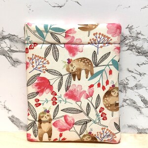 May include: A white fabric pouch with a zip closure features a pattern of sloths hanging from branches with pink flowers and green leaves.