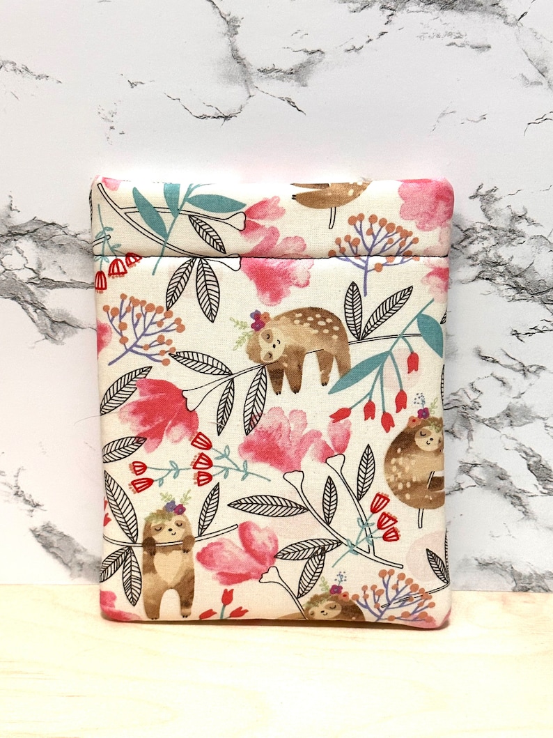 May include: A white fabric pouch with a zip closure features a pattern of sloths hanging from branches with pink flowers and green leaves.
