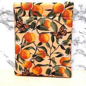 May include: A peach-coloured fabric pouch with a zipper closure. The pouch features a repeating pattern of orange citrus fruit, green leaves, and butterflies.