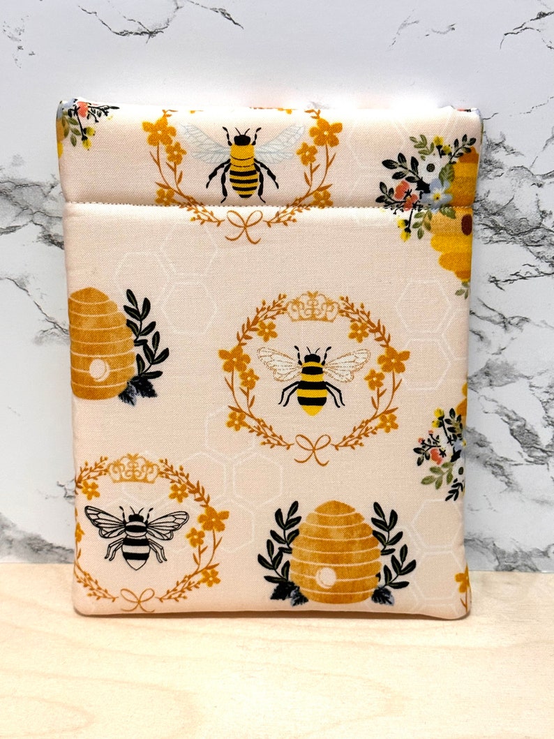 May include: A white fabric pouch with a bee and honeycomb pattern. The pouch has a zipper closure and is ideal for storing small items.
