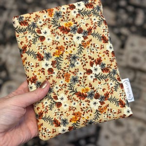 May include: A beige fabric pouch with a floral pattern in shades of orange, red, white, and gray. The pouch has a small white tag with the text "The Book Loft" on it.