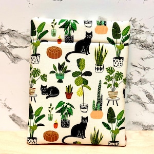 May include: A white fabric pouch featuring a black cat and potted plant design. The pouch has a zipper closure and is ideal for storing small items.