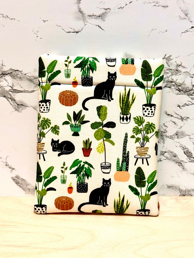 May include: A white fabric pouch featuring a black cat and potted plant design. The pouch has a zipper closure and is ideal for storing small items.