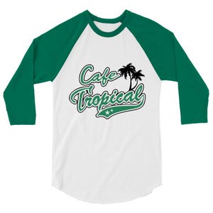 Peut inclure: T-shirt de style baseball blanc et vert avec des manches trois-quarts. Le t-shirt présente le texte "Cafe Tropical" dans une police verte script avec un contour noir, ainsi que deux palmiers et deux étoiles.