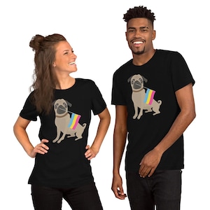 May include: Black t-shirts featuring a cartoon pug wearing a collar and holding a flag with pink, yellow, and blue stripes. The pug is tan and gray. The people in the image are smiling.