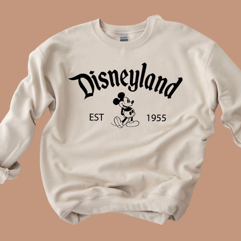 May include: A beige sweatshirt with a black graphic of Mickey Mouse and the text "Disneyland EST 1955".