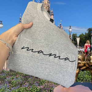 May include: Gray sweatshirt with the word "Disney" in a black and white embroidered script with the word "mama" written in cursive underneath.