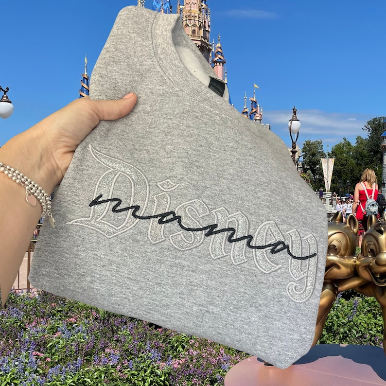 May include: Gray sweatshirt with the word "Disney" in a black and white embroidered script with the word "mama" written in cursive underneath.