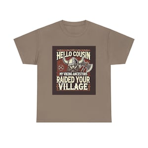 Puede incluir: Una camiseta marrón con un gráfico de un vikingo con un casco con cuernos y sosteniendo un hacha. El gráfico dice "Hello Cousin, My Viking Ancestors Raided Your Village".