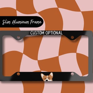May include: Black license plate frame with a custom optional text "CUSTOM OPTIONAL" at the top and a cartoon image of a corgi dog peeking out from the bottom. The frame is set against a background of a wavy checkerboard pattern in brown and pink.