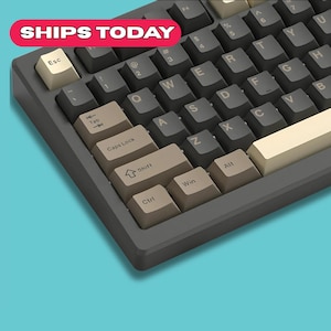 Puede incluir: Primer plano de un teclado mecánico con teclas de color gris oscuro y teclas de acento de color beige claro y blanquecino. El teclado tiene un marco gris oscuro y el texto "SHIPS TODAY" está en una pancarta roja en la esquina superior izquierda.