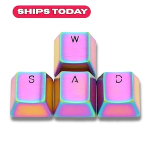 Könnte beinhalten: Schillernde Tastenkappen mit den Buchstaben "W", "A", "S" und "D". Die Tastenkappen haben eine metallische Oberfläche mit Regenbogenfarbeneffekt. Der Text "SHIPS TODAY" befindet sich in einem roten Oval oben.