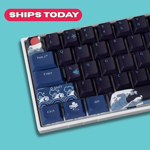 Könnte beinhalten: Eine mechanische Tastatur mit dunkelblauen Tastenkappen und einem weißen Rahmen. Die Tastenkappen zeigen japanische Wellen- und Wolkenmuster mit einer roten Sonnengrafik oben links. Die Tastatur hat den Text "SHIPS TODAY" in einem roten Banner.